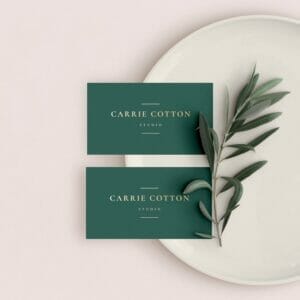 Two green business cards on a plate with eucalyptus leaves.