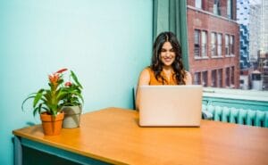 A woman sitting at a desk with a laptop in front of a window.
