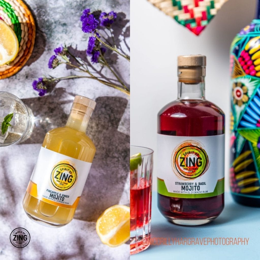 Two bottles of Zing mojito mixers—one pineapple & basil, the other strawberry & basil—displayed beside drinks and colourful props on a textured surface, perfect for your next bottled cocktails marketing campaign.